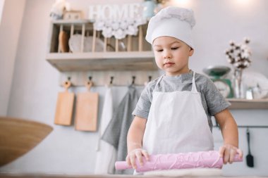 Mutfaktaki yakışıklı çocuk beyaz üniformalı aşçı şefi ve masaların yanında şapka takıyor. Ev yapımı zencefilli ekmek. Çocuk çikolatalı kurabiyeleri pişirdi.
