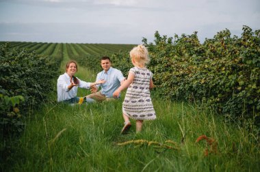 Mutlu bir aile parkta yürüyor. Anne, baba ve kız dışarı çıkıyorlar, ebeveynler kızın elini tutuyor. Çocukluk, ebeveynlik, aile bağları, evlilik kavramı.