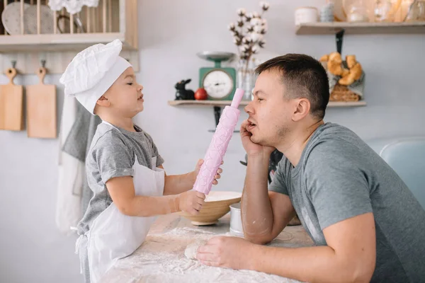 Young man and his son with oven sheet in kitchen. Father with little son on the kitchen