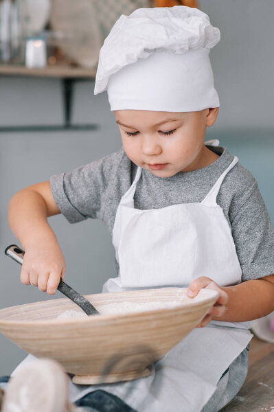 Young boy cute on the kitchen cook chef in white uniform and hat near table. homemade gingerbread. the boy cooked the chocolate cookies