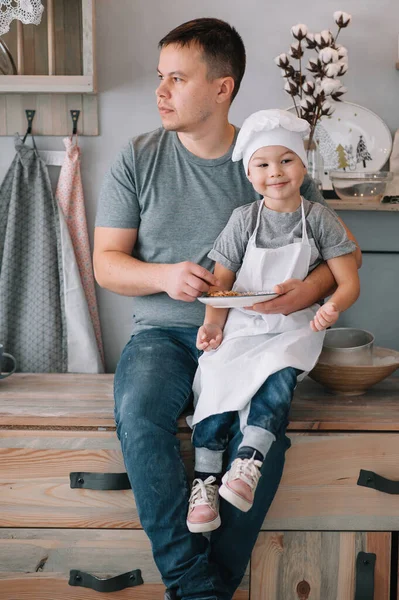 Young man and his son with oven sheet in kitchen. Father with little son on the kitchen