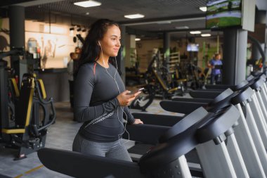 Spor salonunda koşu bandında koşup kulaklıkla müzik dinleyen genç bir kadın. Sağlıklı yaşam tarzı kavramı.