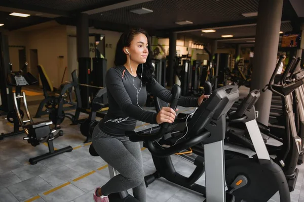 Ung Kvinna Med Hörlurar Gör Övningar Brevpapper Cykel Ett Gym — Stockfoto