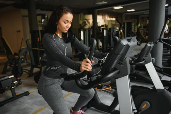 Kulaklıklı Genç Bir Kadın Spor Salonunda Spor Salonunda Kırtasiye Bisikleti — Stok fotoğraf