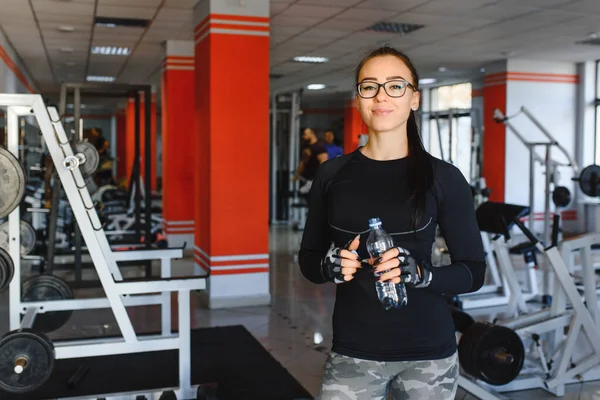 Professional bodybuilding athlete relax after exhausting training. Athlete relax and drink water from sport bottle in gym interior.