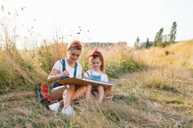 Genç anne ve kızı Anneler Günü 'nde eğleniyor. Güzel kızı olan gülümseyen anne doğayı çizer.