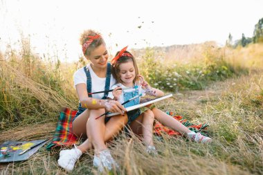 Güzel anne küçük kızıyla resim yapıyor. Küçük kızla resim çizen şık bir kadın. Beyaz tişörtlü ve kot pantolonlu şirin bir çocuk. Anneler Günü