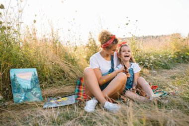 Güzel anne küçük kızıyla resim yapıyor. Küçük kızla resim çizen şık bir kadın. Beyaz tişörtlü ve kot pantolonlu şirin bir çocuk. Anneler Günü