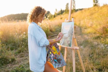 Güzel kadın resim yapıyor. Açık hava oturumu. Sevimli bir kadın gün batımında resim çizer. kız sanatçı