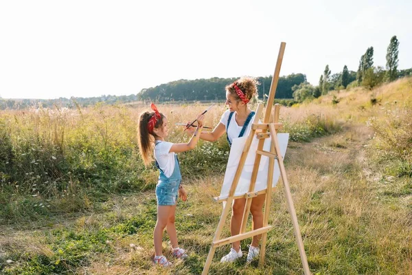 美丽的母亲和她的小女儿一起画画 一个时髦的女人和小女孩一起画这幅画 穿着白色T恤和蓝色牛仔裤的可爱孩子 母亲节 — 图库照片