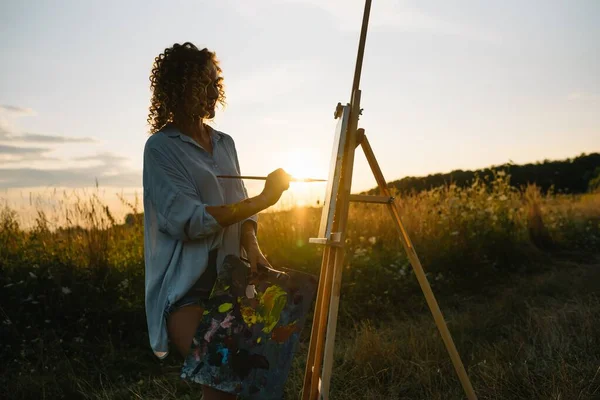 Pretty woman is painting. Open air session. Cute woman draws a picture at sunset. girl artist