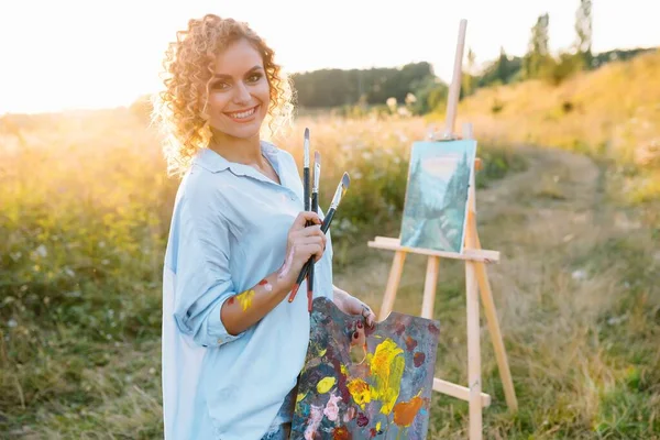 Pretty woman is painting. Open air session. Cute woman draws a picture at sunset. girl artist