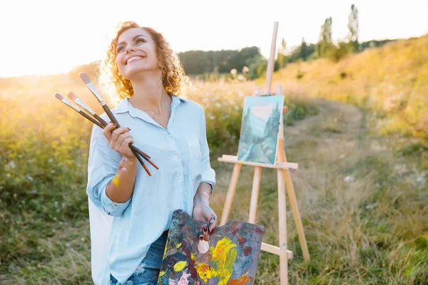 Pretty woman is painting. Open air session. Cute woman draws a picture at sunset. girl artist