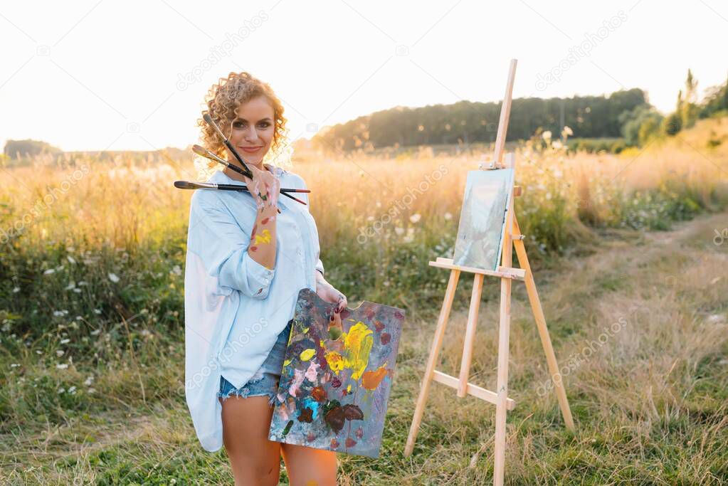 Talented artist in outdoors is mixing paint for her new project while holding brushes.