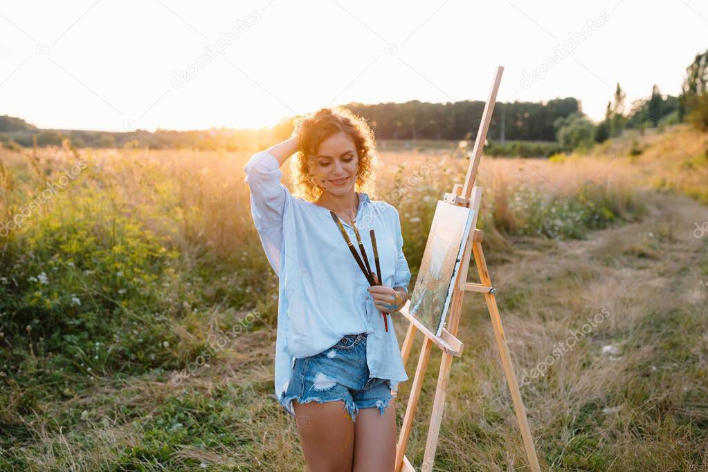 Pretty talented female painter painting on easel, making colorful sketches, creating marine landscape. Beautiful female artist painting with watercolor paints. Creativity and imagination concept.