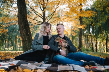 Güz parkında dinlenen genç ve güzel bir çift. Sonbahar konsepti. Sevgili çift kedileriyle dinleniyor..