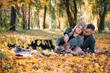 Genç çift sonbahar parkında dinleniyor, erkek kadını kucaklıyor..
