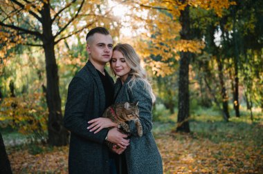 Genç çift sonbahar parkında dinleniyor, erkek kadını kucaklıyor..