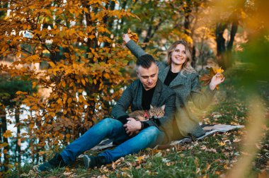 Güz parkında dinlenen genç ve güzel bir çift. Sonbahar konsepti. Sevgili çift kedileriyle dinleniyor..