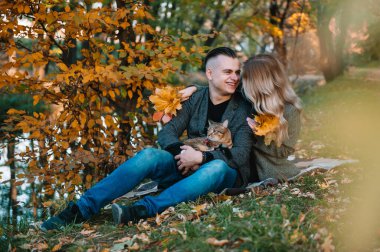 Güz parkında dinlenen genç ve güzel bir çift. Sonbahar konsepti. Sevgili çift kedileriyle dinleniyor..