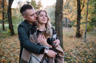 Genç çift sonbahar parkında dinleniyor, erkek kadını kucaklıyor..