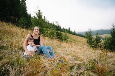 Genç anne ve küçük oğlu seyahat ediyorlar. Anne çocukla gezintiye çıktı, aile gezisi dağlarda. Ulusal Park. Çocuklarla yürüyüş. Aktif yaz tatili.