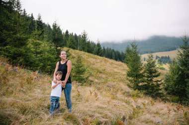 Genç anne ve küçük oğlu seyahat ediyorlar. Anne çocukla gezintiye çıktı, aile gezisi dağlarda. Ulusal Park. Çocuklarla yürüyüş. Aktif yaz tatili.