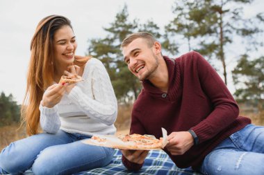 Park bankında oturan ve pizza yiyen genç bir çift. Fast food. Kadın ve erkek gün batımında piknik yapıyorlar. Çocuklar rahatlıyor ve yemeğin tadını çıkarıyor. Yaşam biçimi