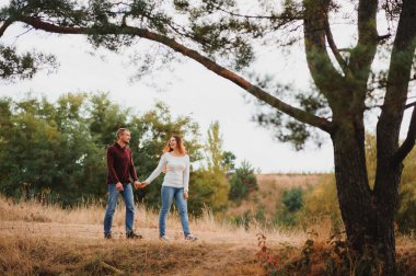Parkta piknik battaniyesine uzanmış aşık bir çift, doğada güzel bir sonbahar gününün tadını çıkarıyor ve sarılıyor.