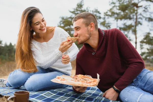 一对年轻的夫妇坐在公园的长椅上 吃着比萨饼 男人们放松和享受食物 生活方式 — 图库照片