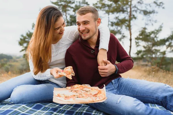 Couple in love lying on a picnic blanket in a park, enjoying beautiful autumn day in nature and cuddling