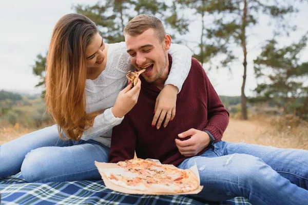 一对年轻的夫妇坐在公园的长椅上 吃着比萨饼 男人们放松和享受食物 生活方式 — 图库照片