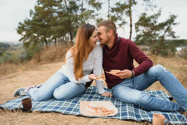 一对年轻的夫妇坐在公园的长椅上 吃着比萨饼 男人们放松和享受食物 生活方式 — 图库照片