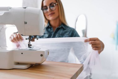 Gülümseyen moda tasarımcısı iş yerinde kameraya bakıyor, terzi, nakış işçisi ya da terzi masasında oturuyor renk kumaşları pantonu ve nakış desenleri ile duvarda, portre