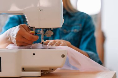 Dikiş makinesi, pembe kumaş ve kadın eli.