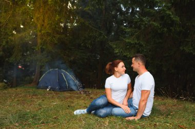Dışarıda kamp yapan ve çadırda oturan romantik bir çift. Mutlu adam ve kadın romantik bir kamp tatilindeler..