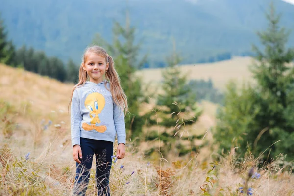 かわいい子供の女の子は山の背景に草の中の牧草地に横たわっている 幸せな子供は山の中で休息している 幸福と屈託のないコンセプト — ストック写真
