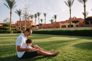 Yakışıklı baba ve küçük tatlı oğlu yeşil çimenlikte eğleniyor ve oynuyorlar. Mutlu aile kavramı. Aile hayatı olan güzel doğa manzarası. Aile birlikte dinleniyor. Babalar Günü