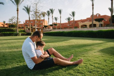 Yakışıklı baba ve küçük tatlı oğlu yeşil çimenlikte eğleniyor ve oynuyorlar. Mutlu aile kavramı. Aile hayatı olan güzel doğa manzarası. Aile birlikte dinleniyor. Babalar Günü