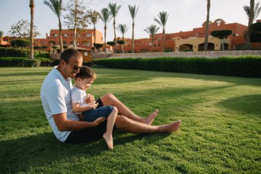 Yakışıklı baba ve küçük tatlı oğlu yeşil çimenlikte eğleniyor ve oynuyorlar. Mutlu aile kavramı. Aile hayatı olan güzel doğa manzarası. Aile birlikte dinleniyor. Babalar Günü