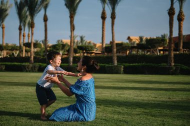 Şık bir anne ve yakışıklı bir oğul yeşil çimlerde eğleniyor. Mutlu aile kavramı. Aile hayatı olan güzel doğa manzarası. Mutlu bir aile birlikte dinleniyor. Anneler Günü