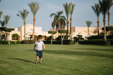 Tatlı çocuk, güneşli bir günde yeşil çimlerde koşup doğada kovalamaca oynuyor..