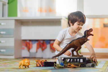 Anaokulunda bir sürü oyuncak etrafında dinozorlarla oynayan sevimli bir çocuk.