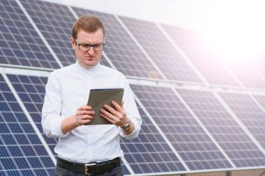 Güneş enerjisi. Güneş panellerinin yanındaki elektrik santrallerine beyaz gömlekli genç iş adamı..