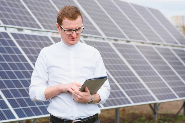 Portrait of man with a tablet in his hands standing near the solar panels station. Green ecological power energy generation. Solar station development concept. Home construction.
