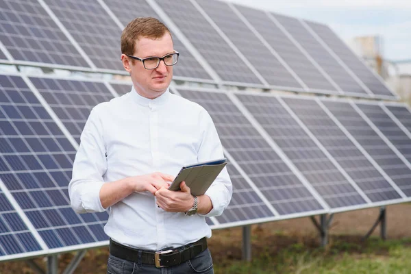 Portrait of man with a tablet in his hands standing near the solar panels station. Green ecological power energy generation. Solar station development concept. Home construction.