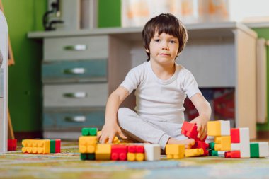 Sevimli küçük çocuk evde küp inşa ederek oynuyor, yerde yatıyor..