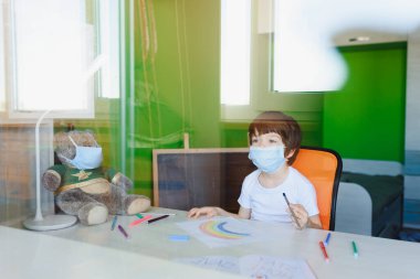Koronavirüs salgını sırasında maskeli çocuk evde gökkuşağı boyuyor. Hepimiz iyi olalım. Sosyal medya kampanyasında evde kal. Çocuklar gökkuşağını kovalıyor