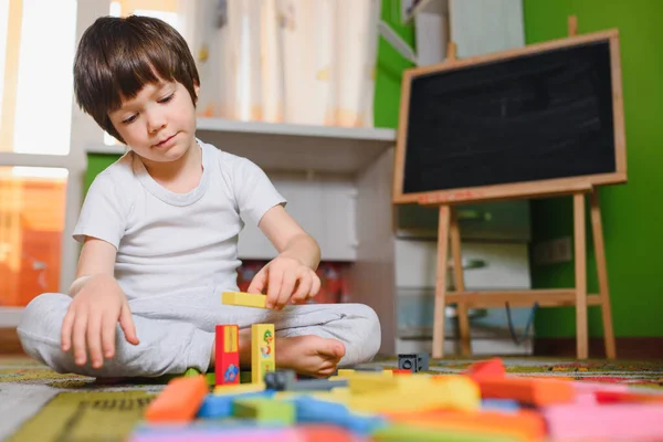 Little sad thoughtful bored toddler boy playing colorful building blocks alone at home during quarantine. development game. Loneliness at self isolation period