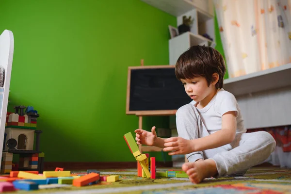 Little sad thoughtful bored toddler boy playing colorful building blocks alone at home during quarantine. development game. Loneliness at self isolation period